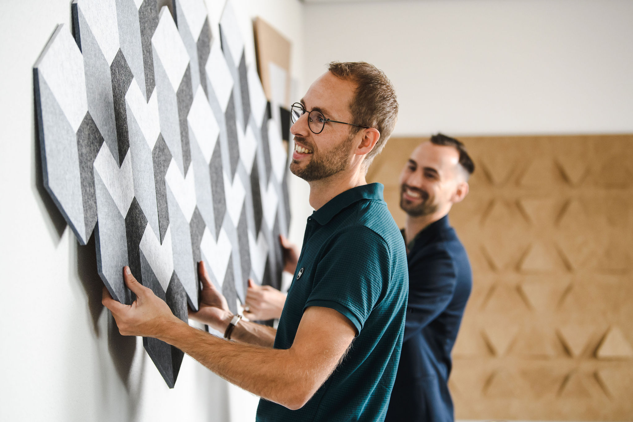 Twee medewerkers van Viltr monteren een wand van grijze viltpanelen